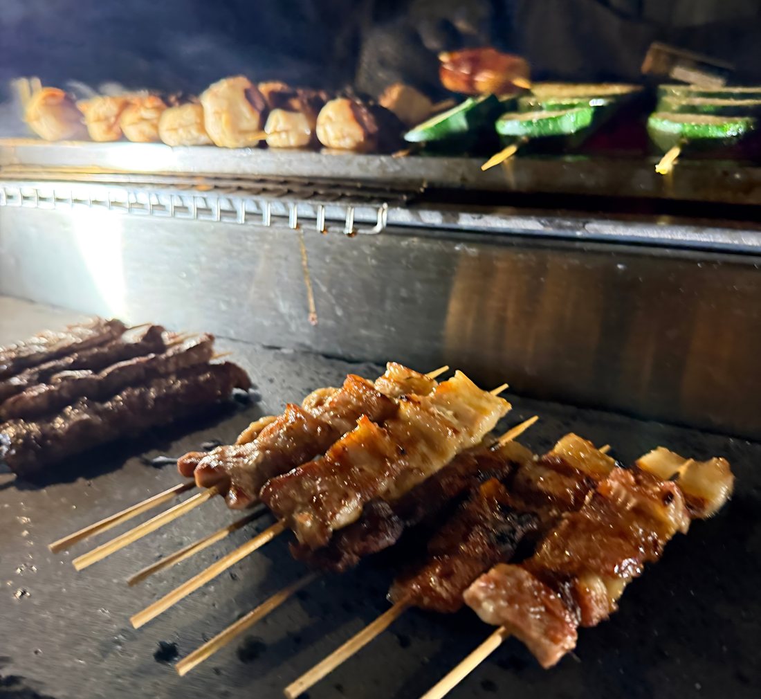Freshly grilled pork and beef yakitori skewers resting beside a live charcoal grill